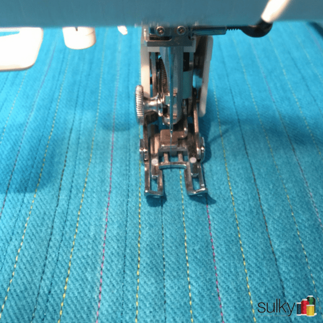 Close-up of sewing machine stitching parallel lines on blue fabric.