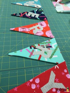 Colorful fabric bunting flags laid out on a green cutting mat.