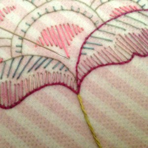 Close-up of embroidery with pink and red thread on fabric.