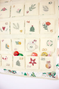 A fabric advent calendar with numbered pockets and Christmas-themed decorations.