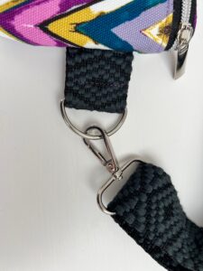Close-up of a black woven strap with a metal clip and colorful fabric.