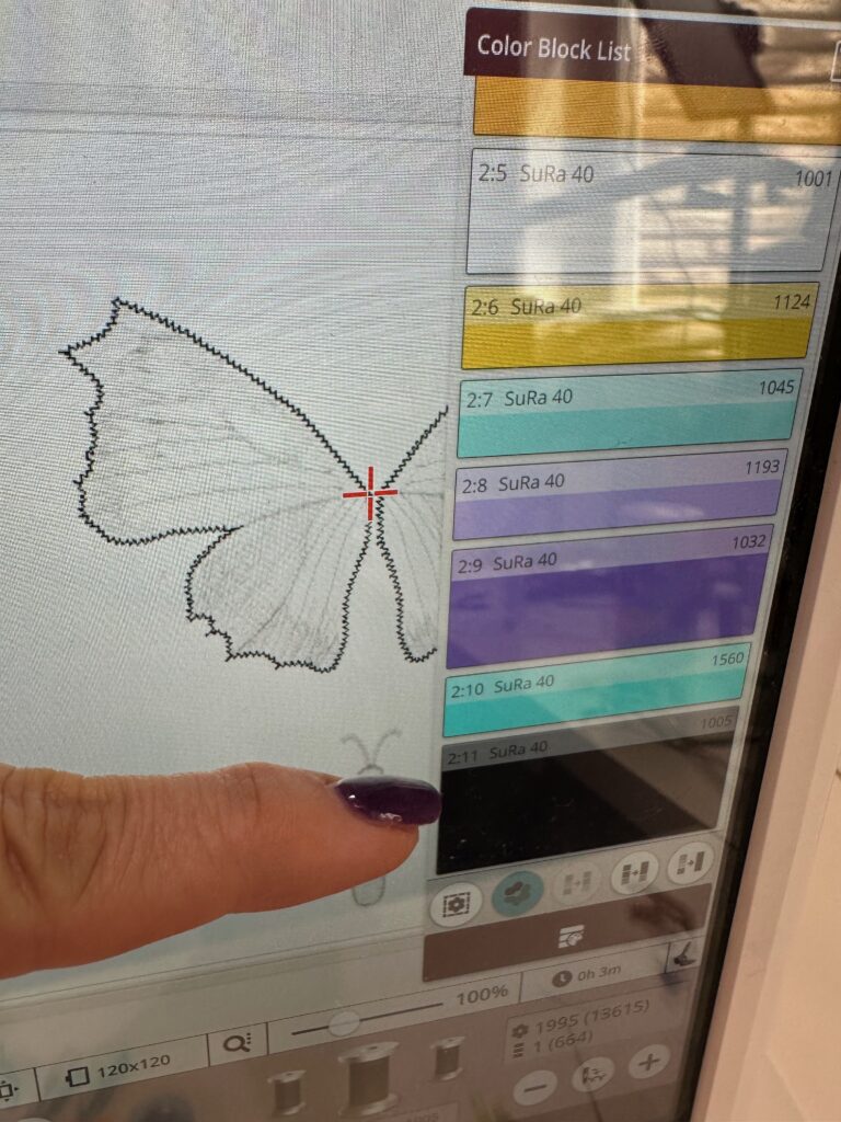 last step of Butterfly Wings design on machine screen with finger indicating color