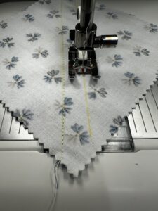 Close-up of sewing machine stitching floral fabric with pins.