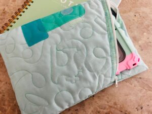 Quilted fabric with stitched letters and a blue-green patch.